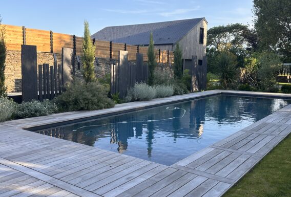 Piscine rectangulaire avec terrasse bois, brise-vue design et végétation méditerranéenne - Réalisation pisciniste Angers